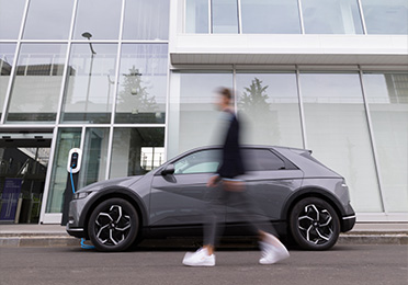 Muž prechádza pred elektromobilom zaparkovaným pri modernej budove