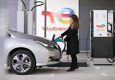 Žena v kabáte dobíja elektromobil na dobíjacej stanici TotalEnergies