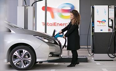 Žena v kabáte dobíja elektromobil na dobíjacej stanici TotalEnergies