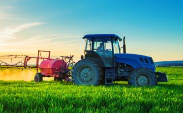 Poľnohospodársky traktor striekajúci pesticídy postrekovačom na poli