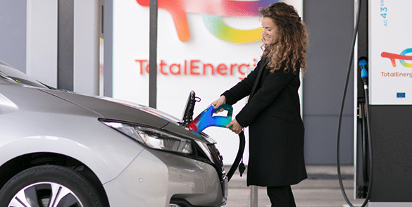 Žena v kabáte dobíja elektromobil z nabíjacej stanice TotalEnergies